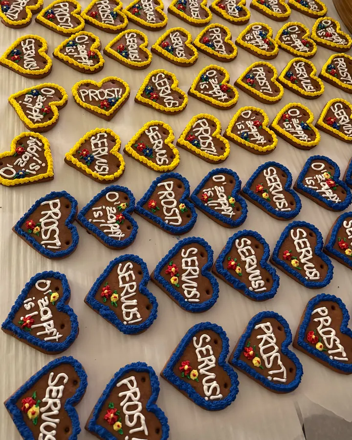 Rows of gingerbread hearts with yellow and blue piped borders, iced with the words Prost, Servus and O’zapft is