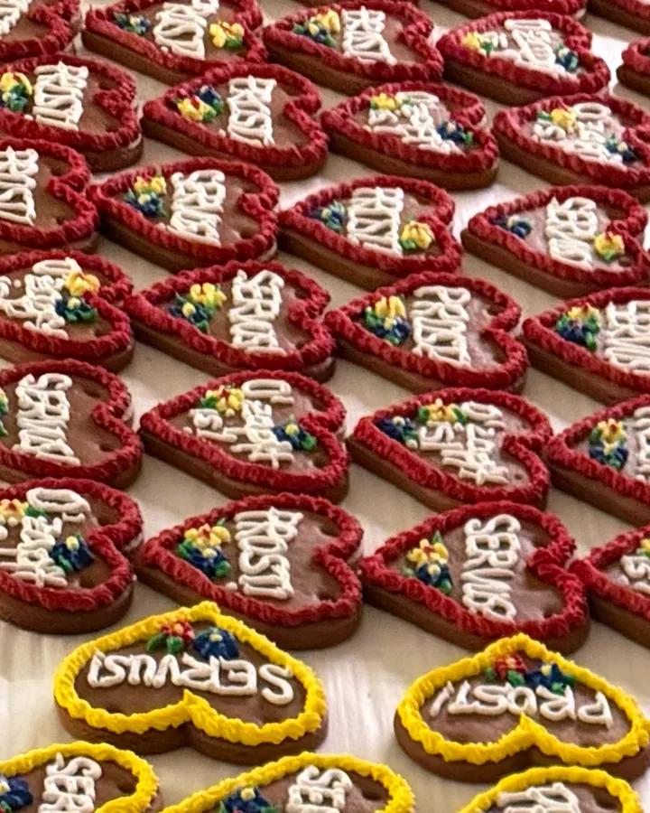 Close-up of gingerbread hearts with red piped borders and white icing, a row of yellow-bordered hearts in front