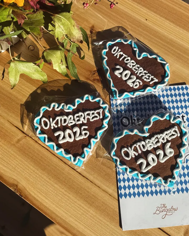 Blue-and-white iced Oktoberfest gingerbread hearts on a wooden table beside The Bungalow card and autumn flowers